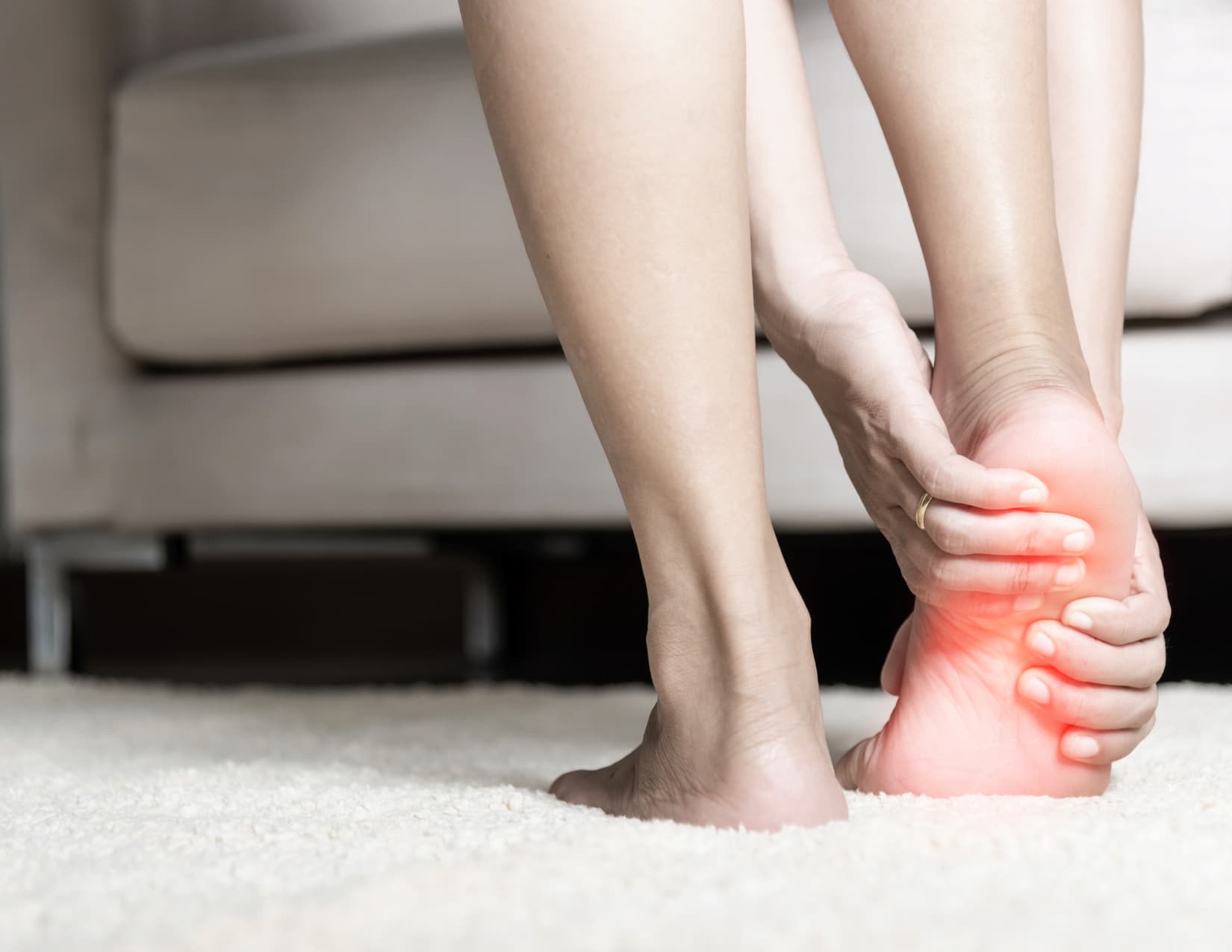 Person grips the sole of their foot, highlighted in red, experiencing pain.