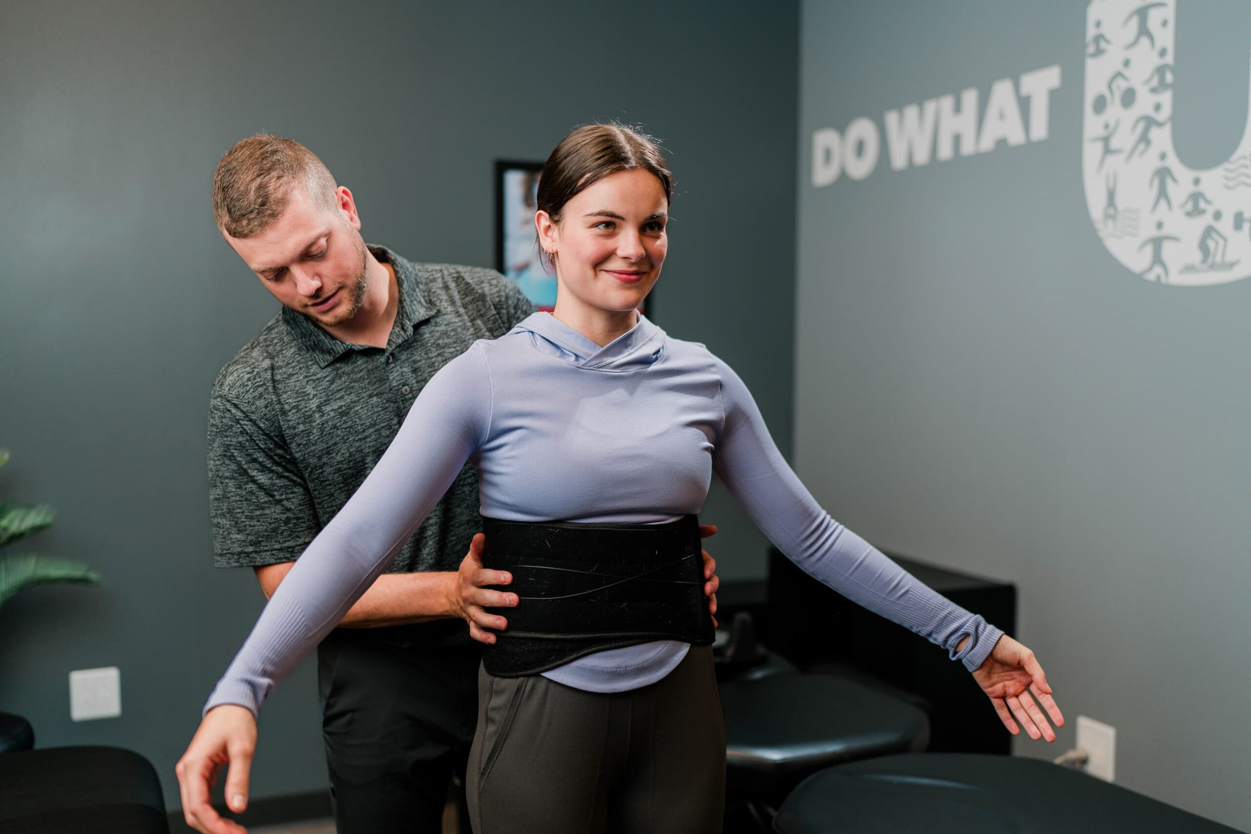 Patient stands with arms out as a practitioner fits them with a back brace.