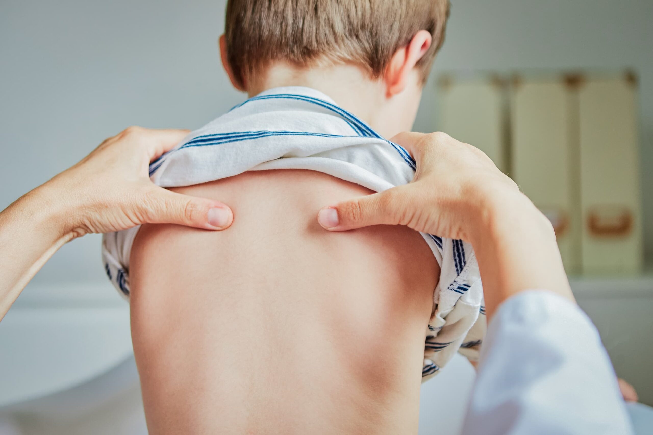 Practitioner examines child's back by pressing on their shoulder blades.