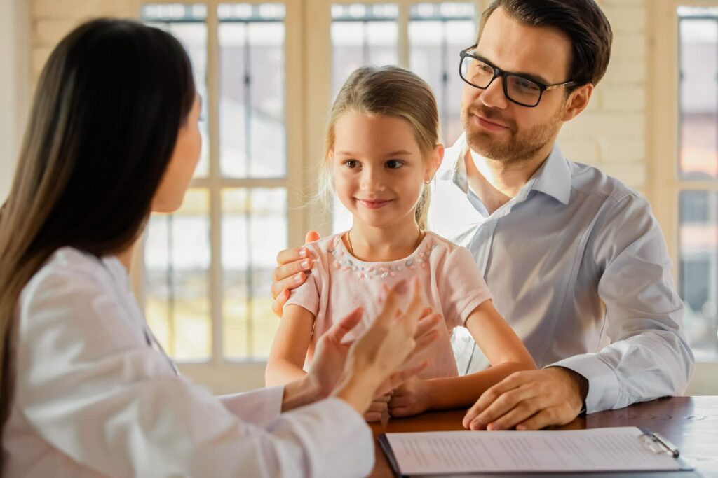 Father and daughter sit at a desk, listening intently as a practitioner describes their exam results.