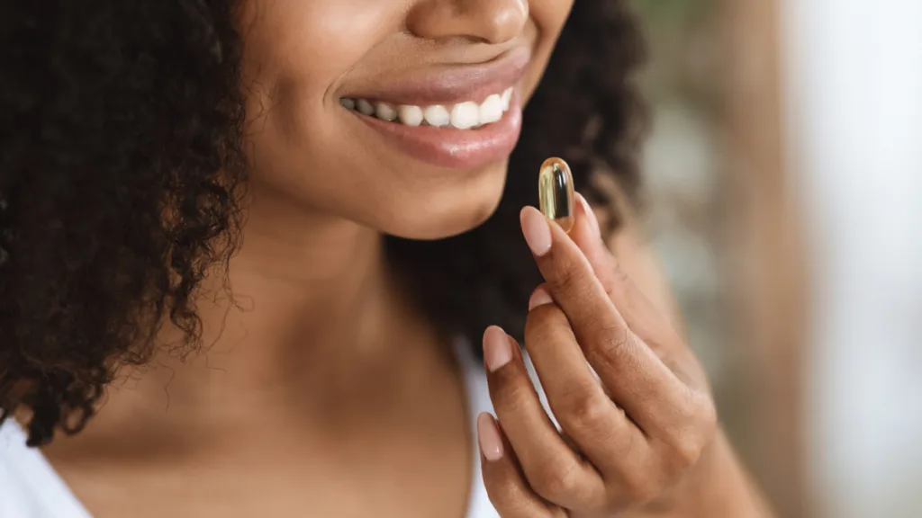 A woman smiling as she holds a supplement capsule near her mouth, preparing to take it.